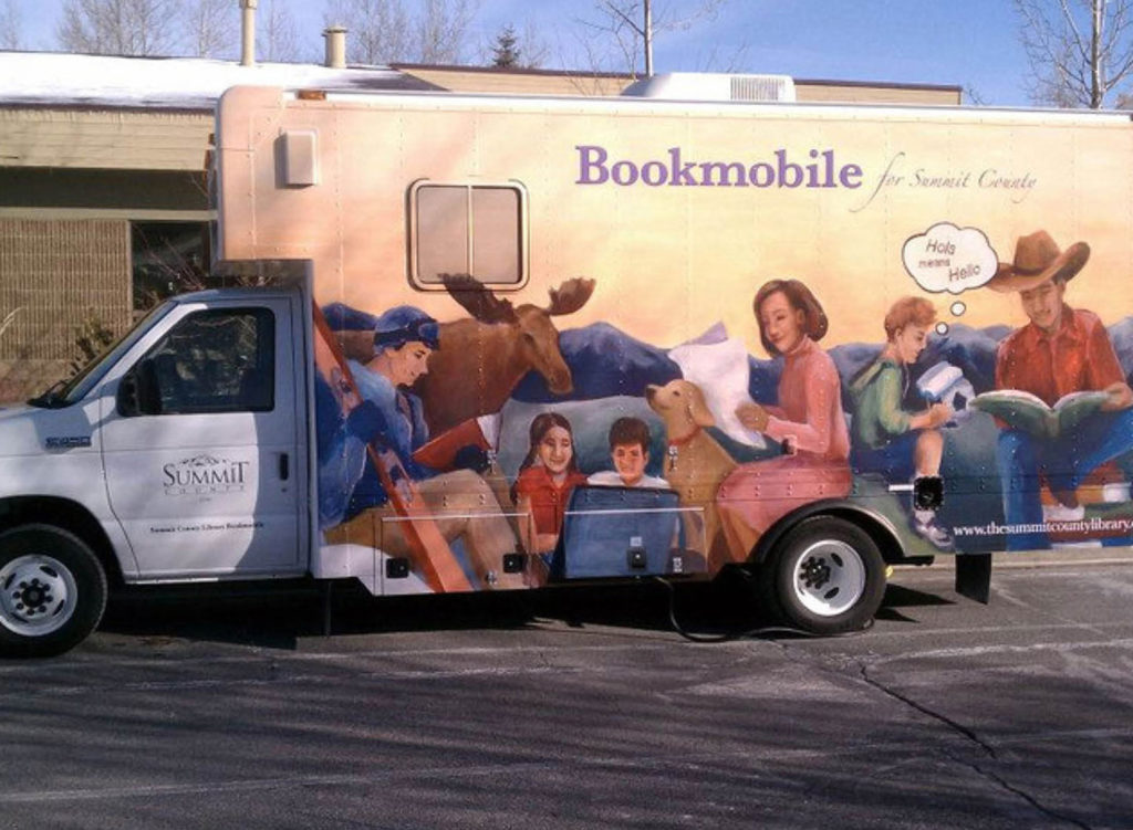 Summit County Library Bookmobile featuring a colorful mural of people, animals, and nature reading together, parked outside a library building on a snowy day.