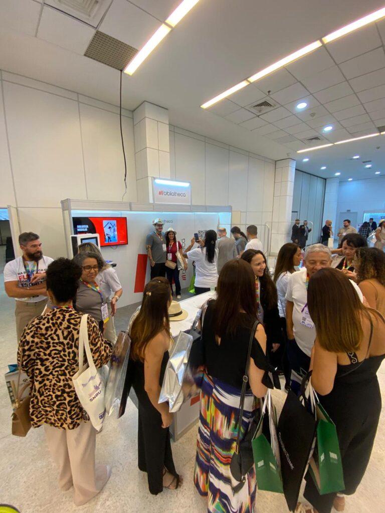 Visitantes interagem com o estande da Bibliotheca no SNBU 2025, interagindo com as soluções tecnológicas como selfCheck, antenas de segurança e Hublet.