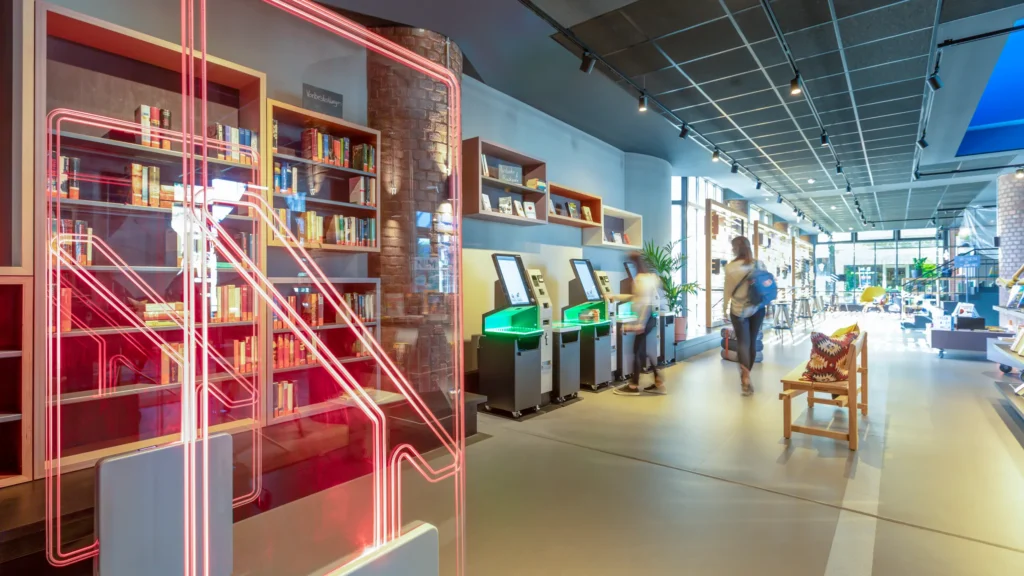 Modern library interior with RFID security gates and Bibliotheca self-checkout kiosks at Kalk Library in Cologne, Germany.